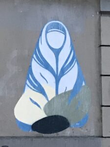 Sticker graffiti of a woman with a blank face sitting cross-legged; part of one knee has been removed